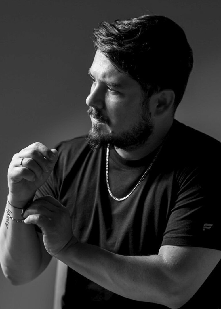 Man in a black t-shirt in side profile with his hands raised near his chest in a studio portrait