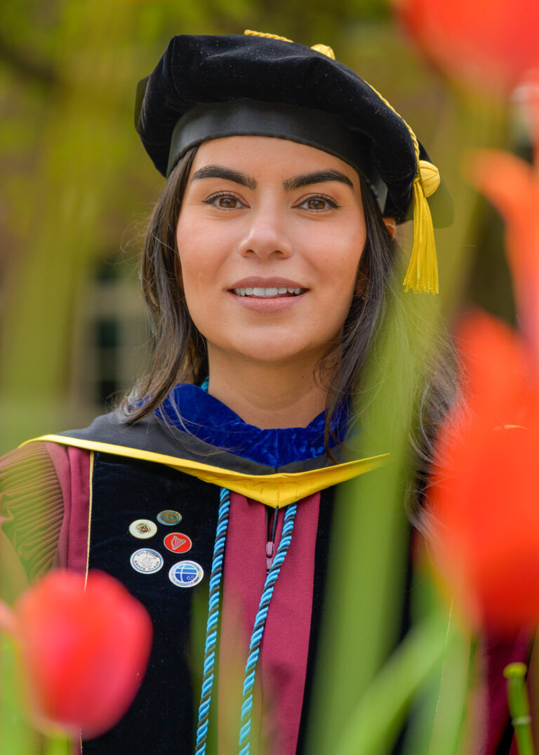 Smiling graduate in a cap and academic regalia framed by red tulips