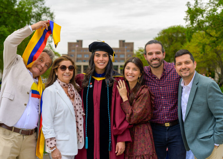 Graduate in cap and gown posing with family and friends outdoors