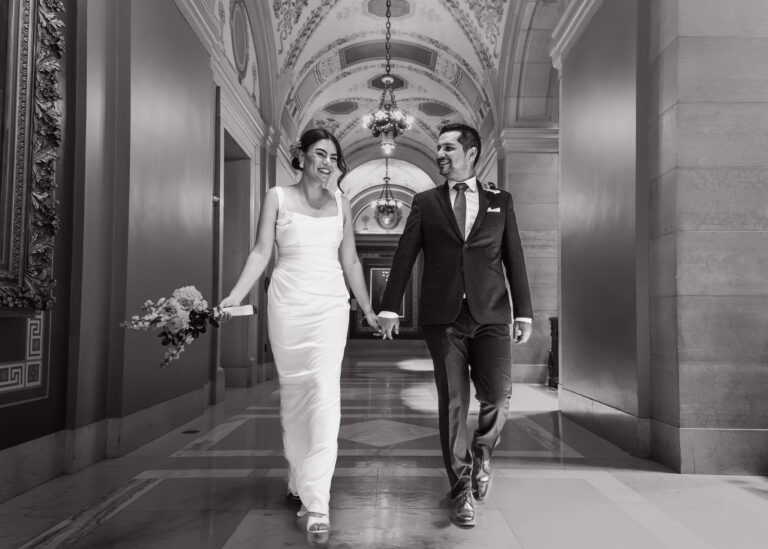 Black and white photo of a bride and groom walking down an arched corridor