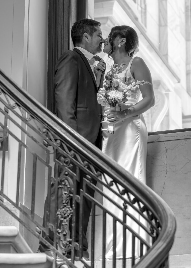 Couple on a curved staircase with a wrought iron railing, in black and white