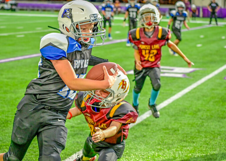 Young football players in a close play on a green field, one carrying the ball
