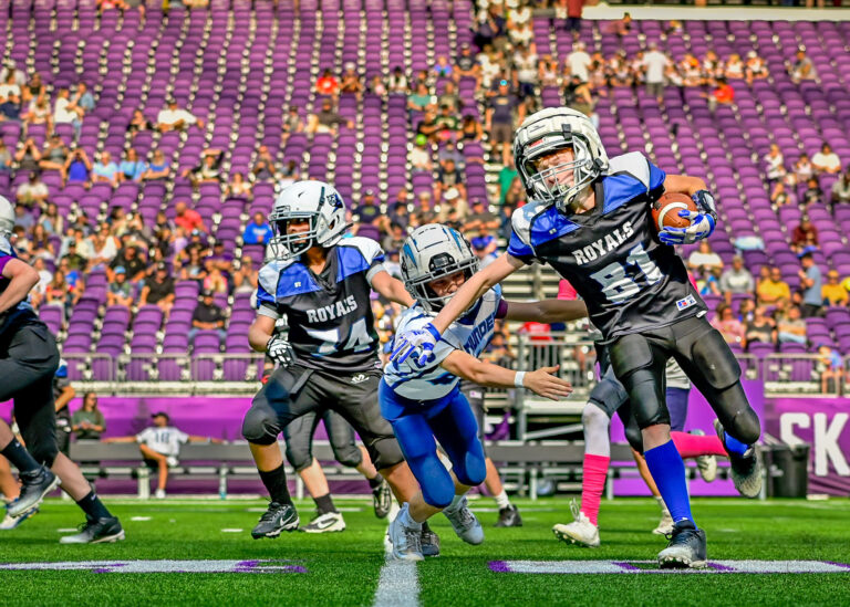 Football players in blue running a play in front of purple stadium seats