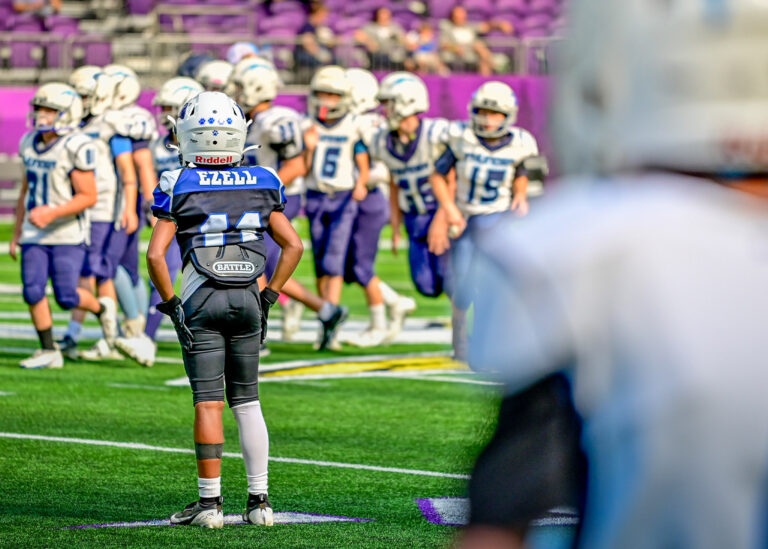 Football players in blue and white uniforms on the field with a blurred player in the foreground