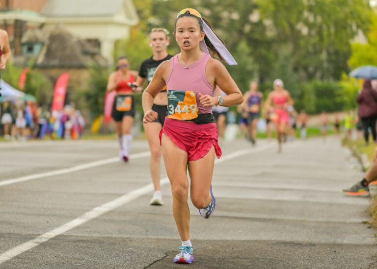 Woman in a pink top running in a road race with other runners behind her