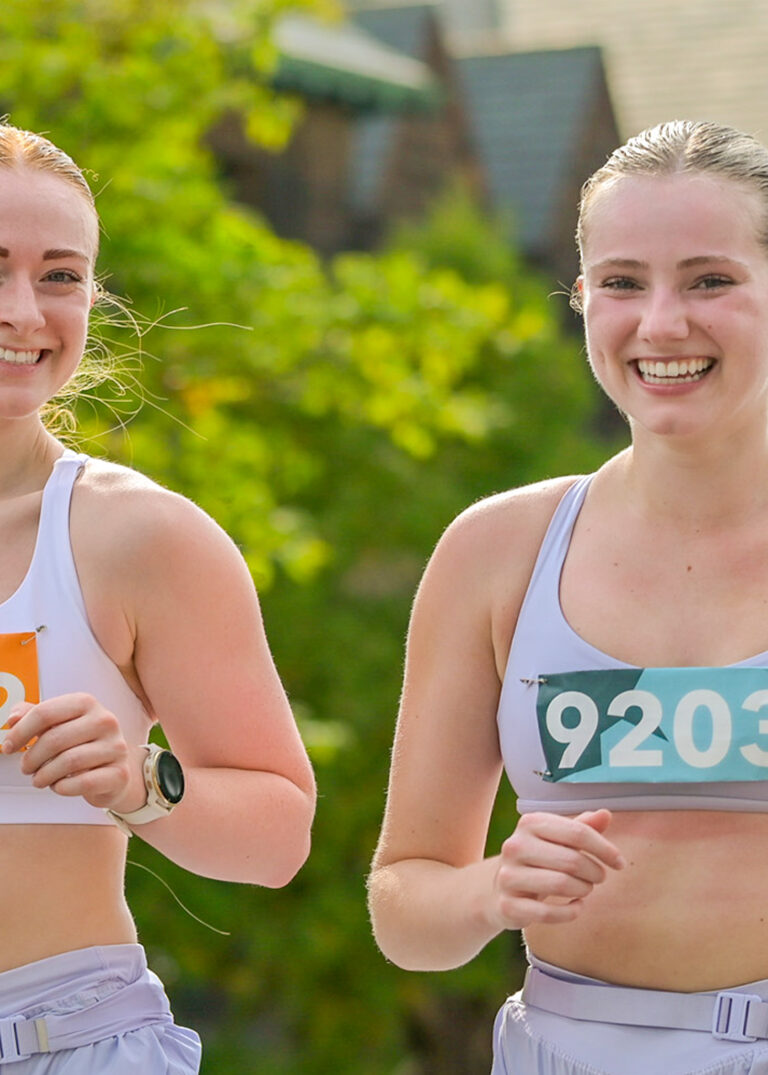 Close-up of two smiling women runners wearing race bibs