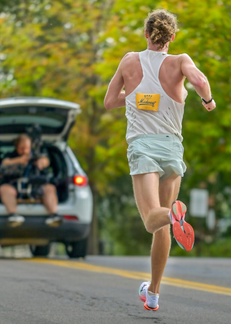 Runner in a light tank top running on a road with parked cars behind