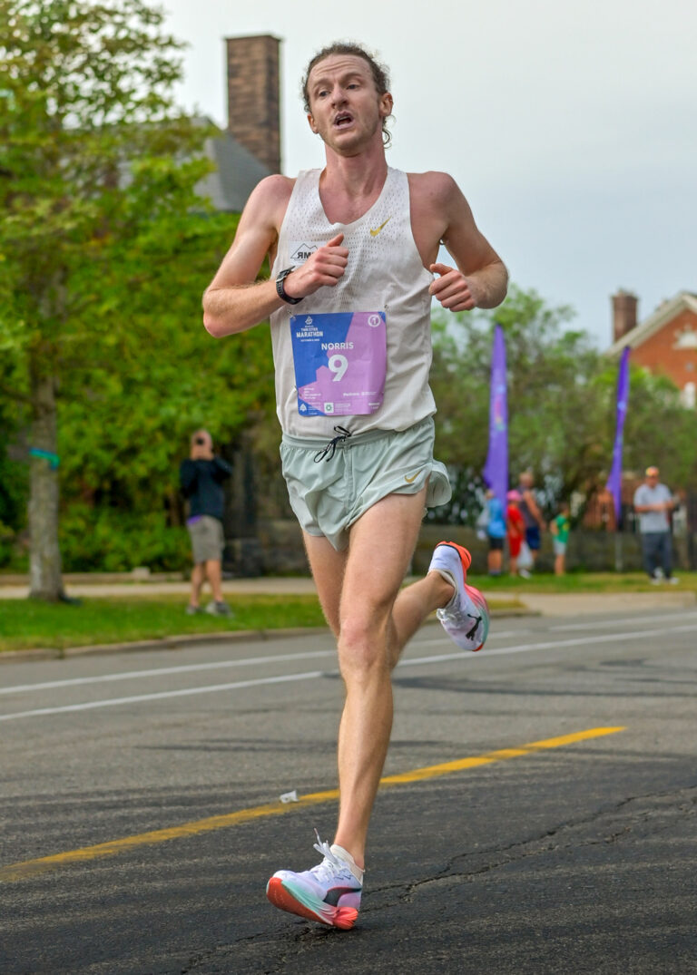 Runner in a white tank top running down a road during a race