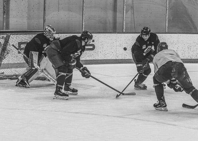 Hockey players battle for the puck in front of the net in black and white