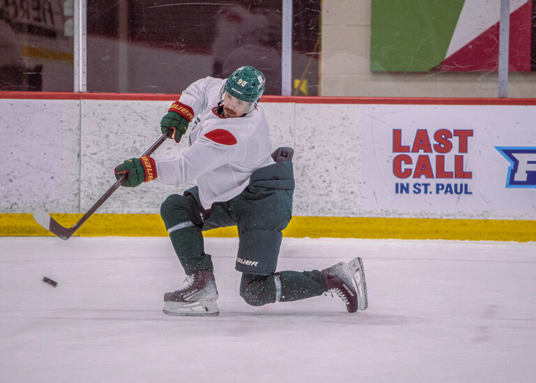 Hockey player in a white jersey taking a knee with the puck on the ice