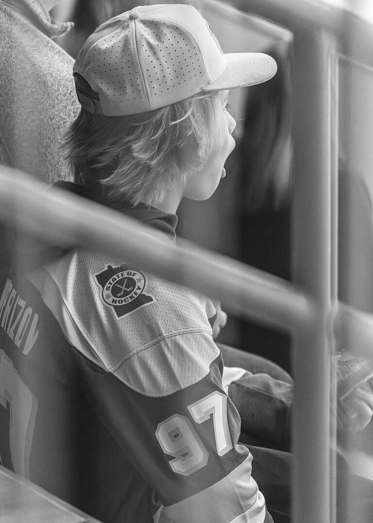 Young hockey fan in a team jersey leaning on the rink boards