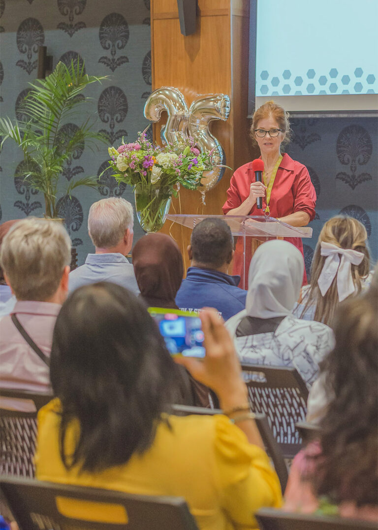 Speaker at a podium with flowers addressing the audience at an anniversary event