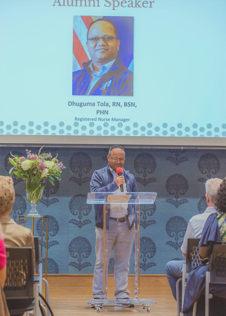 Presenter speaking at a podium in front of a presentation screen at a corporate event