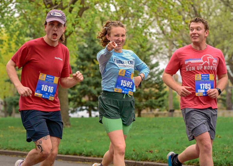 Three runners in red and blue shirts running together on a park road