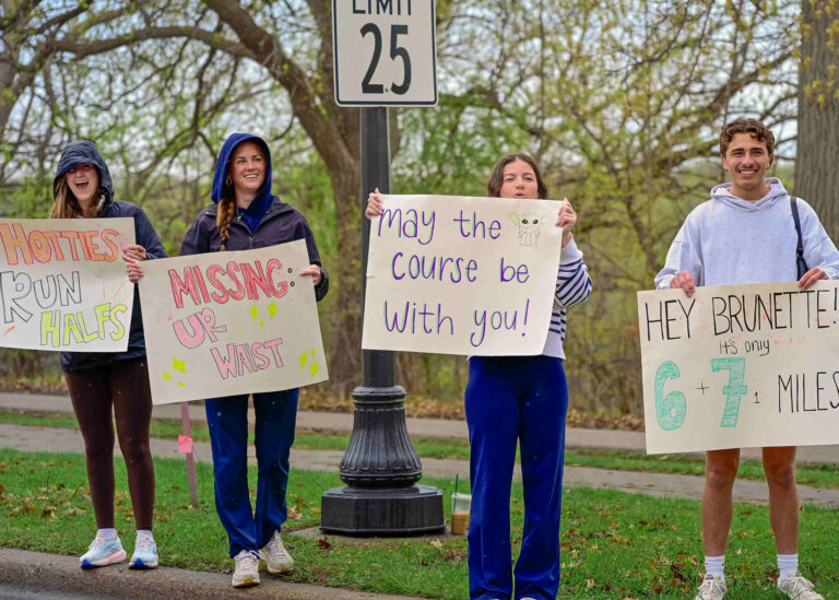 Spectators holding handmade encouragement signs along the race course