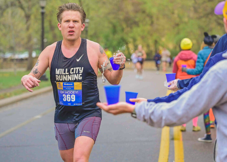 Runner in a black singlet and race bib taking a cup from a volunteer