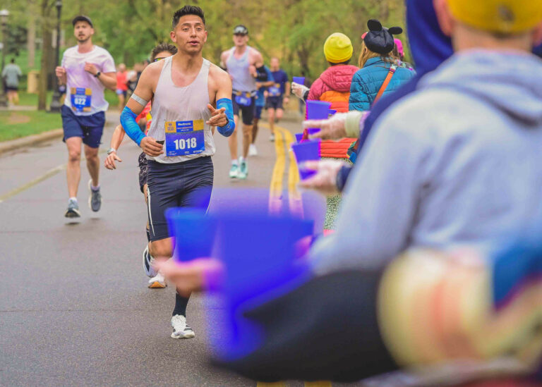 Runners reaching for cups at a water station during a race