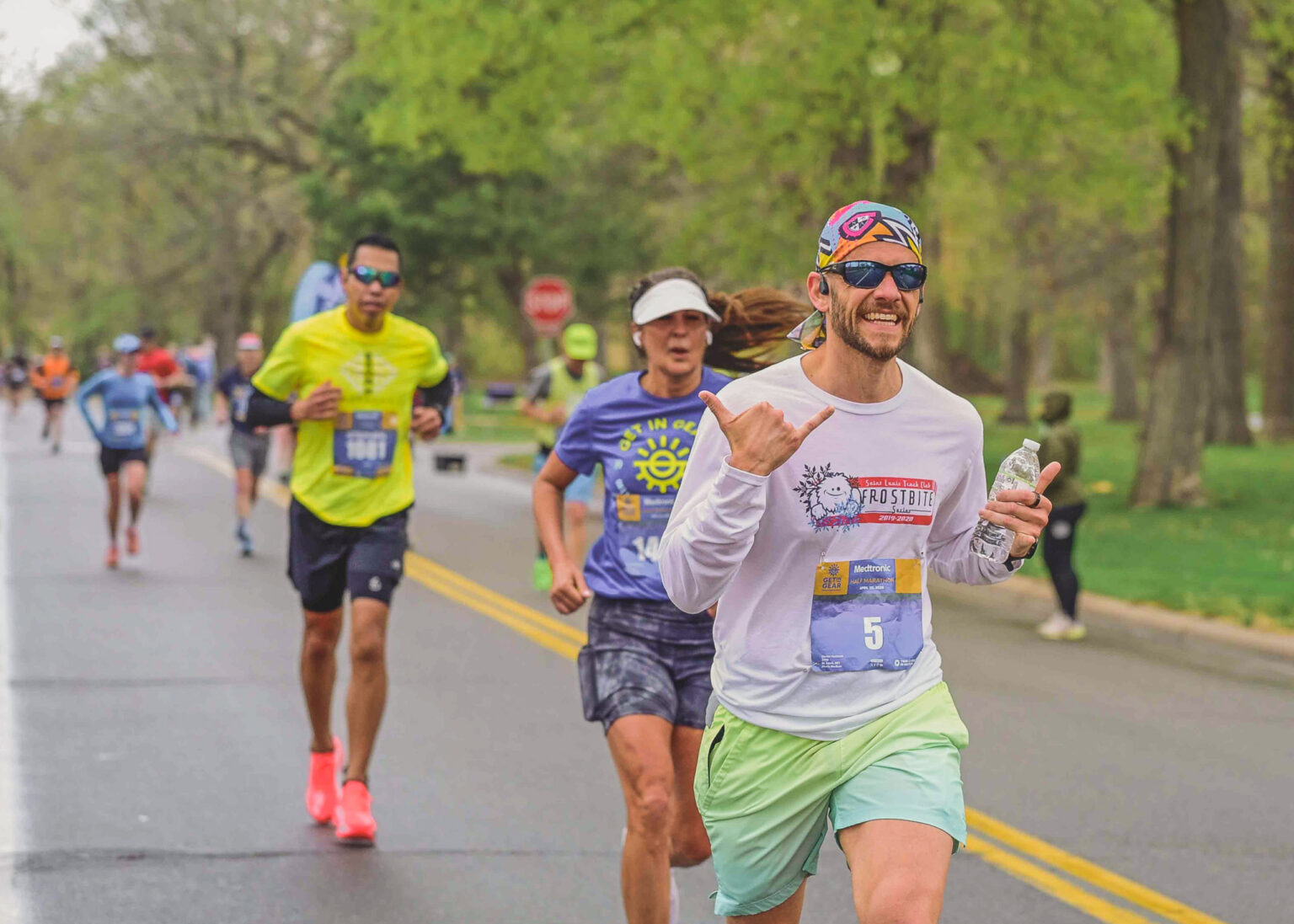 Runners on a park road during a race, one in a yellow shirt and another smiling