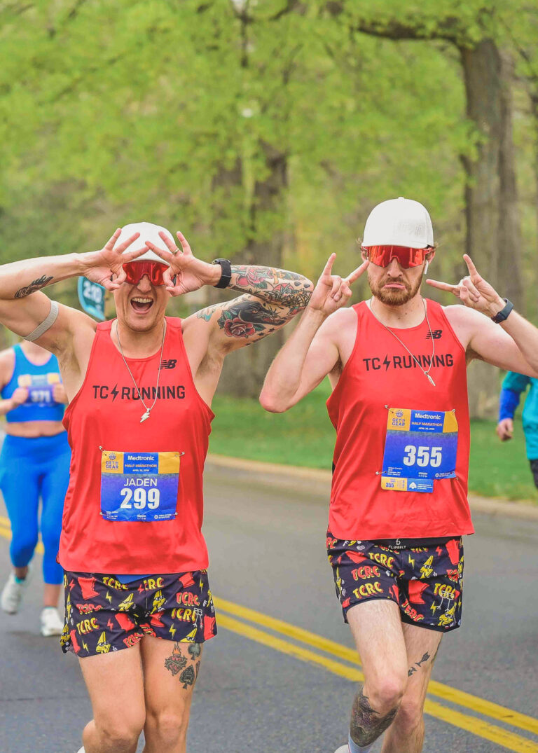 Two runners in red tank tops with arms raised running together