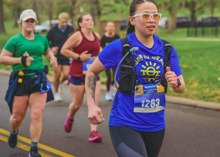 Two runners in blue shirts and race bibs running side by side