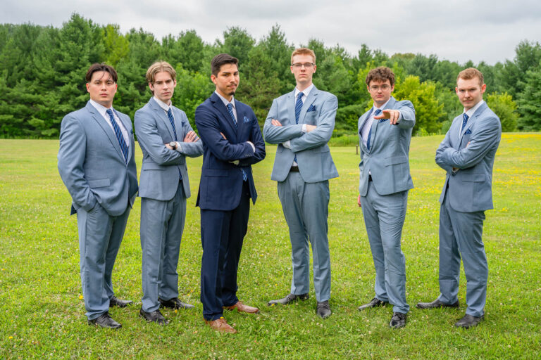 Six groomsmen in light blue suits posing together on a green lawn