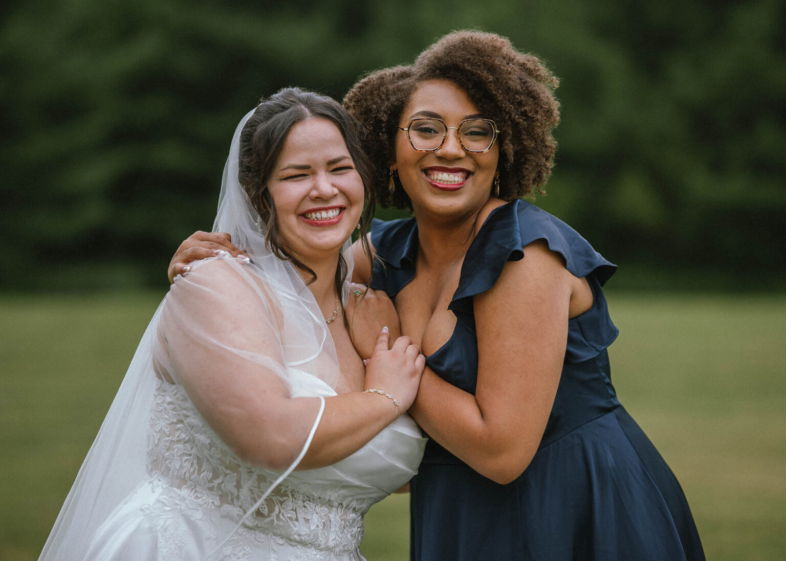 Bride and bridesmaid in a dark blue dress laughing cheek to cheek