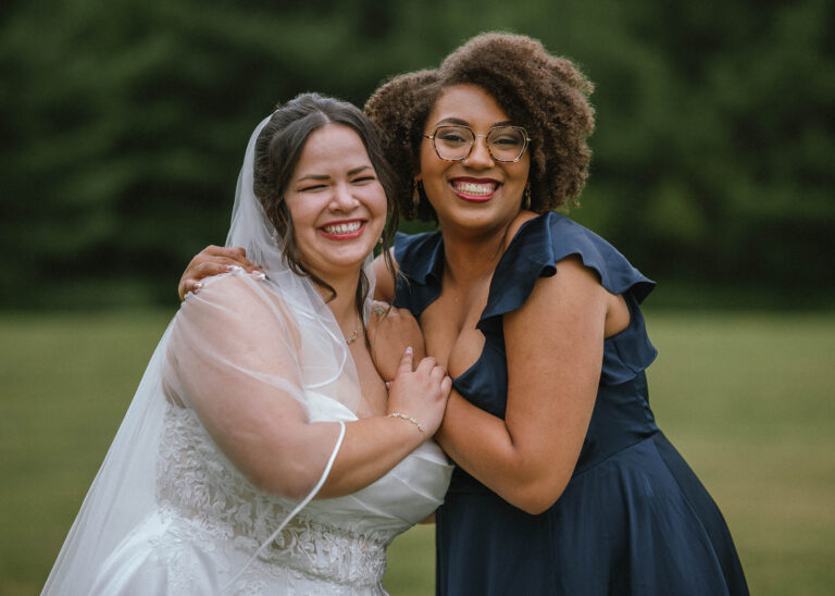 Bride and bridesmaid in a dark blue dress laughing cheek to cheek