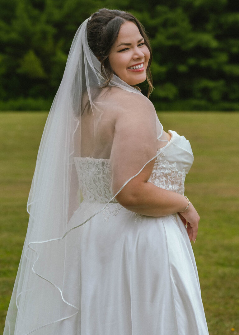 Bride in a white wedding dress and veil posing on a green lawn