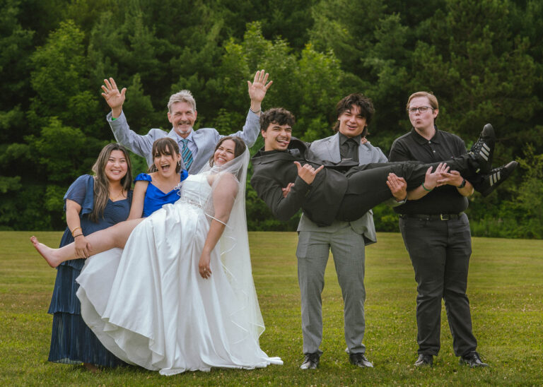 Wedding party playfully lifting the bride on the lawn