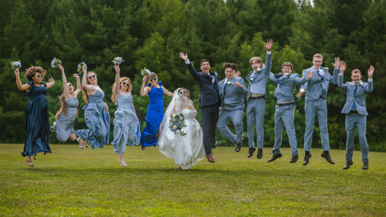Wedding party in light blue attire jumping and posing together on a lawn