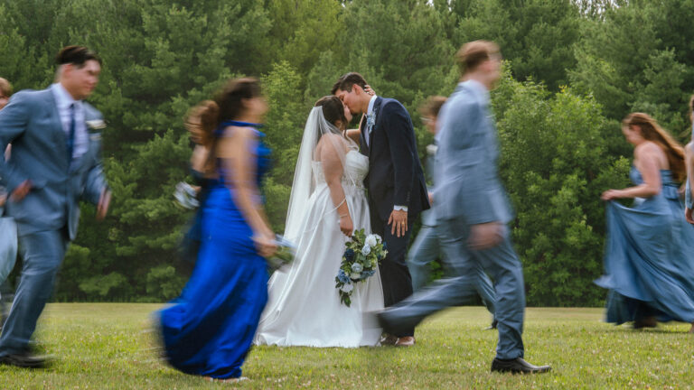Bride and groom with wedding guests in blue attire walking across a lawn