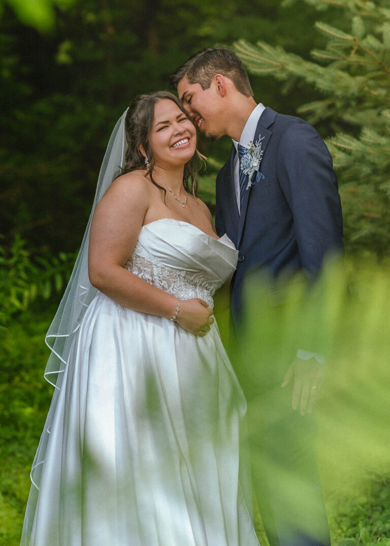 Bride and groom embracing outdoors with soft blurred greenery in the foreground