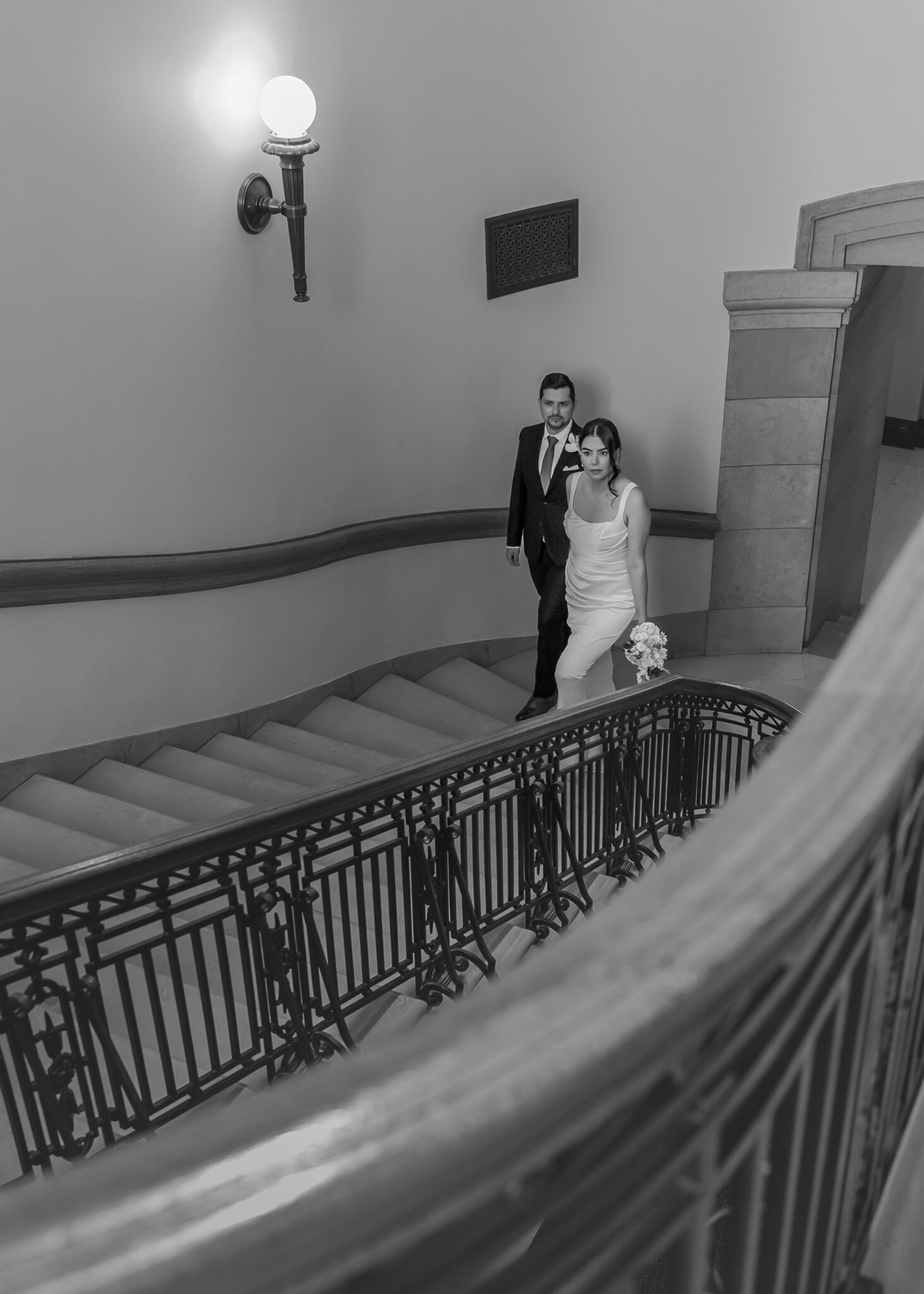 Bride and groom standing on a curved staircase landing, in black and white