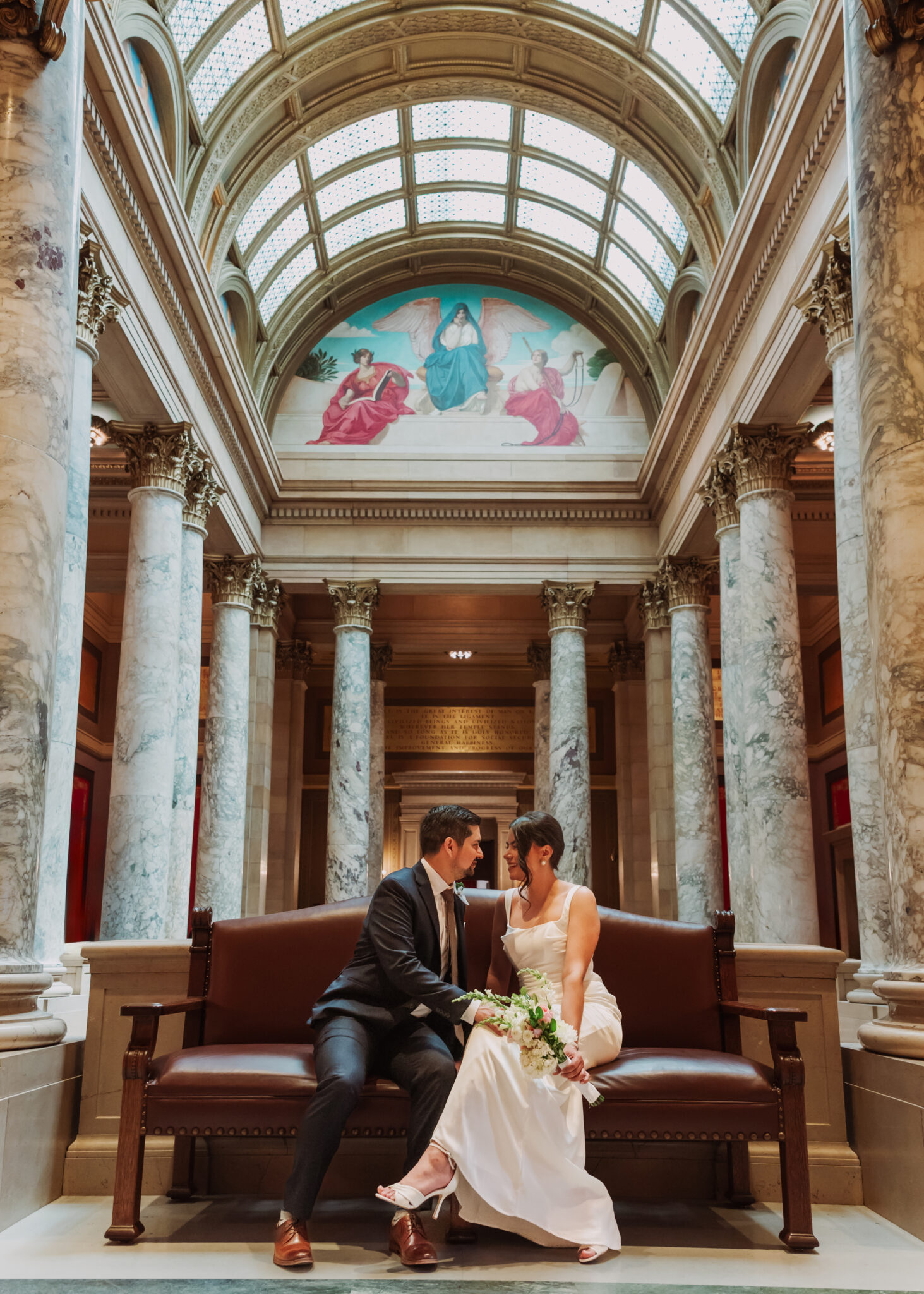 Couple sitting together on a red bench in a grand hall beneath a stained glass dome