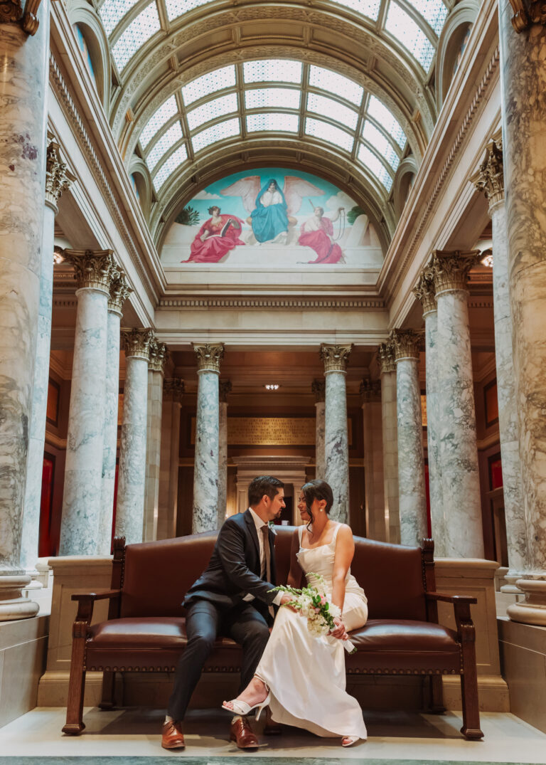 Couple sitting together on a red bench in a grand hall beneath a stained glass dome