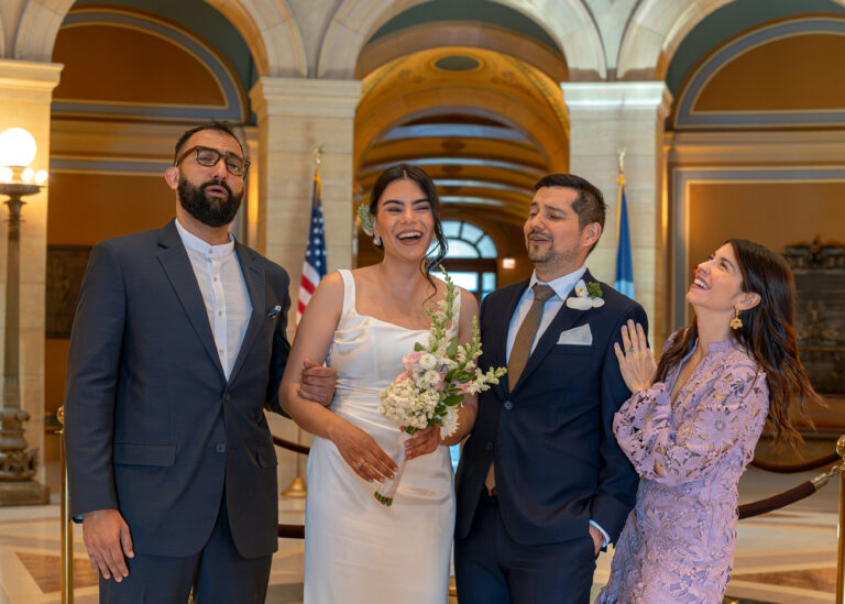 Bride and groom laughing with two guests in a marble hall with flags