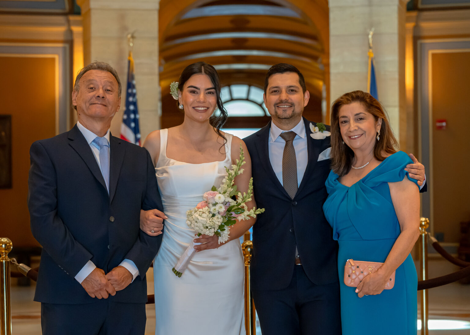 Bride and groom arm in arm with the groom's parents in a marble hall