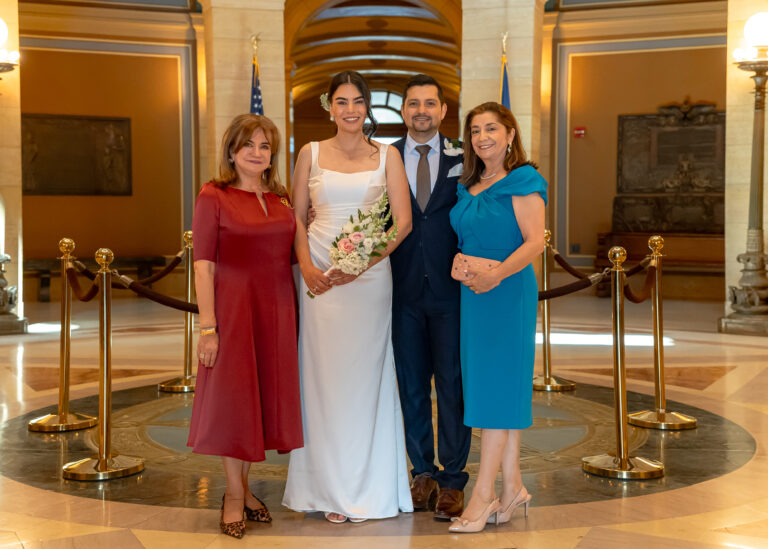 Bride and groom standing with two family members in a marble hall with gold stanchions