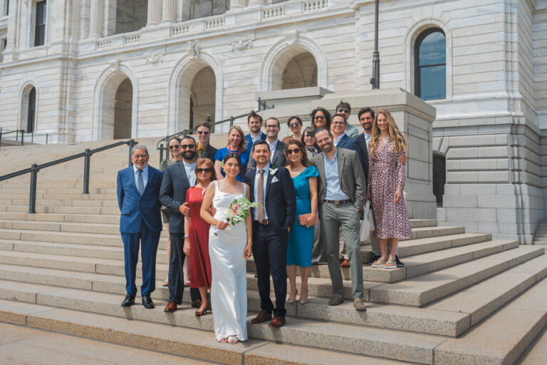 Wedding party gathered on stone steps outside a grand white marble building